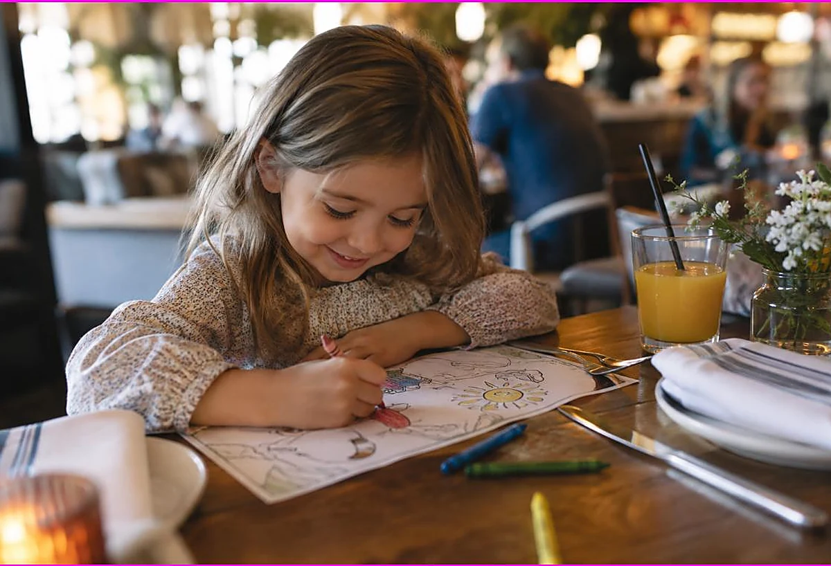 Child coloring a kids activity placemat with crayons at a restaurant table, coloring pages to keep kids busy at restaurants
